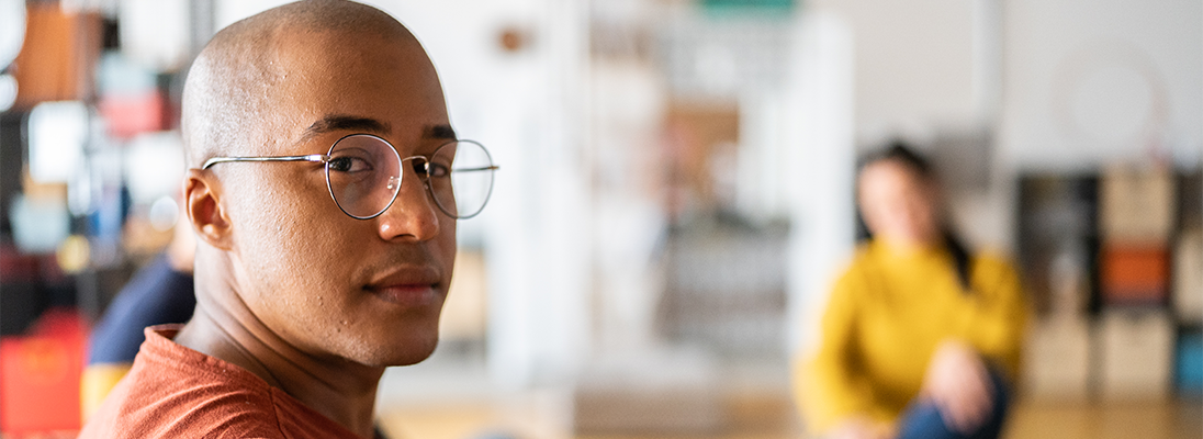 Man with glasses looking directly at the camera Man looking at the camera with another person in the background